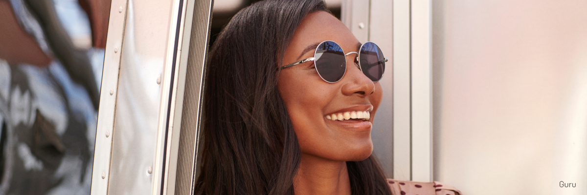A woman smiling wearing round sunglasses
